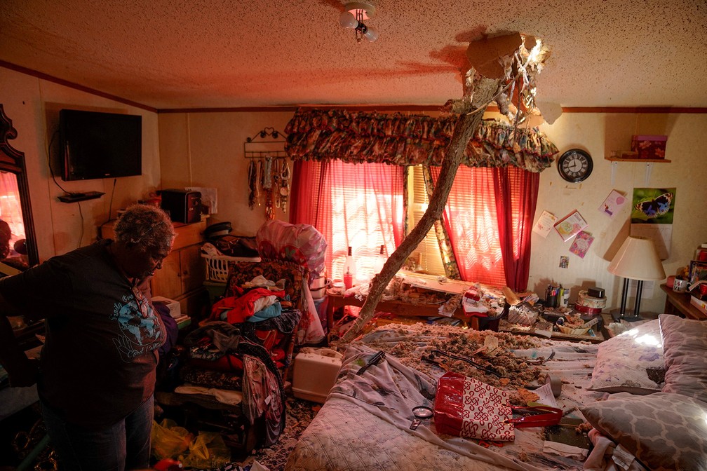 Ester Johnson-El, de 62 anos, encontra um enorme galho de árvore cravado pelo teto sobre sua cama ao verificar os estragos deixados pela passagem de um tornado em Wynne, Arkansas. Ela conta que deixou a casa com a nora, o sobrinho e o neto no meio da tempestade — Foto: Cheney Orr/Reuters