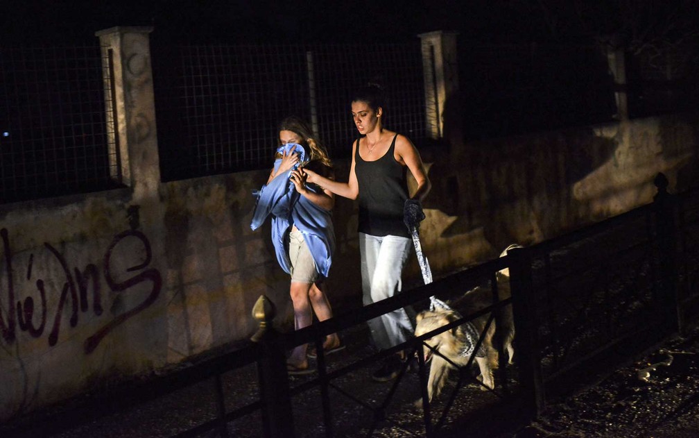 Duas mulheres e um cão fogem dos incêndios em Mati (Foto: Angelos Tzortzinis / AFP Photo)