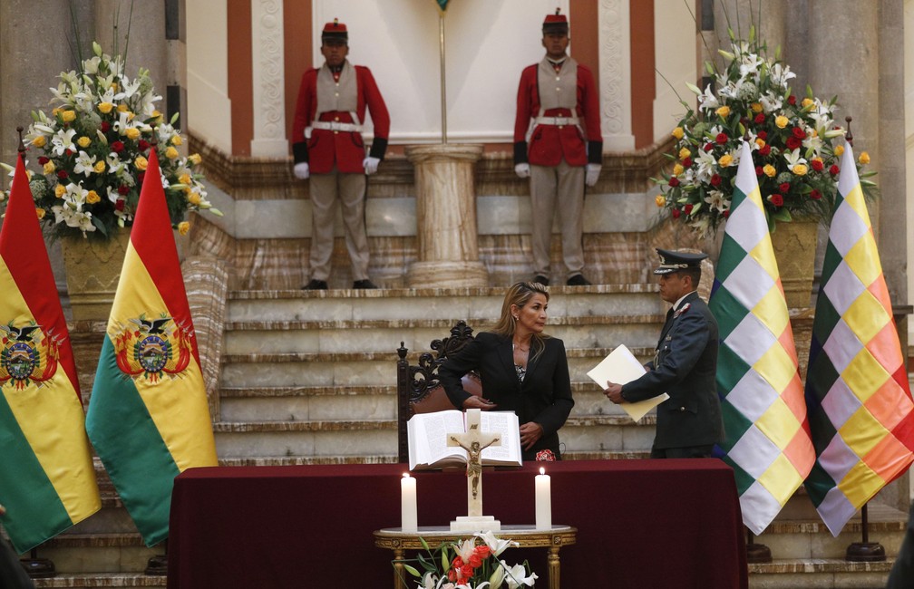 Ambas consideradas símbolos nacionais pela constituição, a bandeira da Bolívia (E) e a wiphala (D) são colocadas atrás de mesa de onde discursou Jeanine Añez, proclamada presidente boliviana, na quarta-feira (13) — Foto: Juan Karita/AP Photo