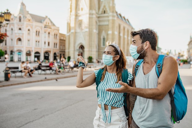 Two tourists wearing face masks and backpacks. They are walking and smiling (Foto: Getty Images)