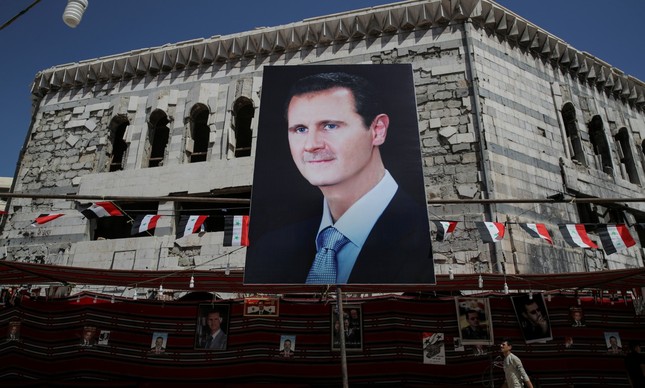 Um homem carrega um pôster com uma imagem de Assad em Damasco 