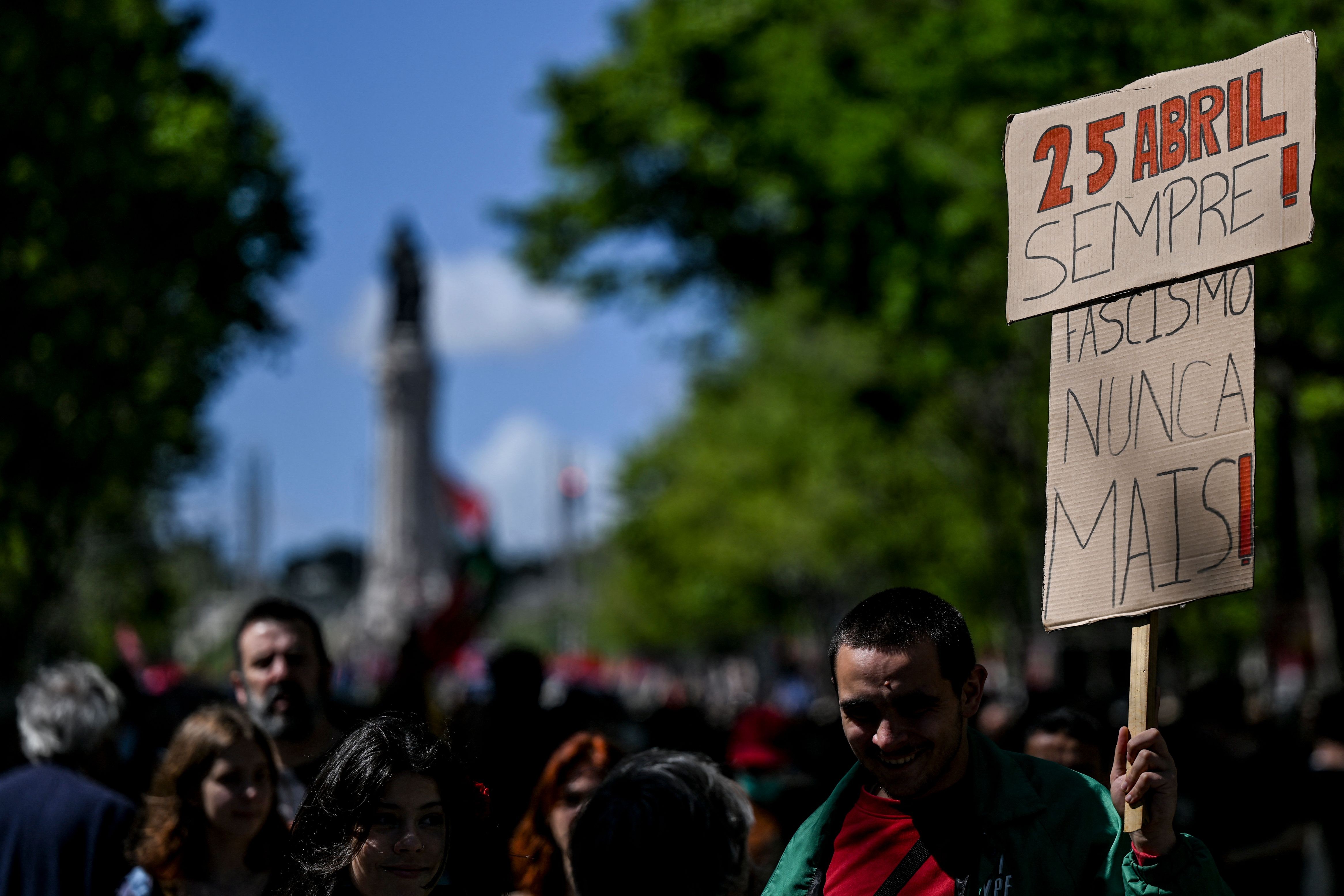 Homem exibe cartaz ao lado de outros participantes da celebração do 25 de Abril em Lisboa