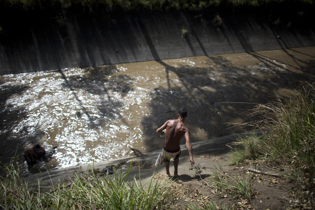 Homem desce barranco para ir 'garimpar' o Rio Guaire, conhecido por carregar águas pluviais, esgoto e resíduos industriais (Foto: Ariana Cubillos)