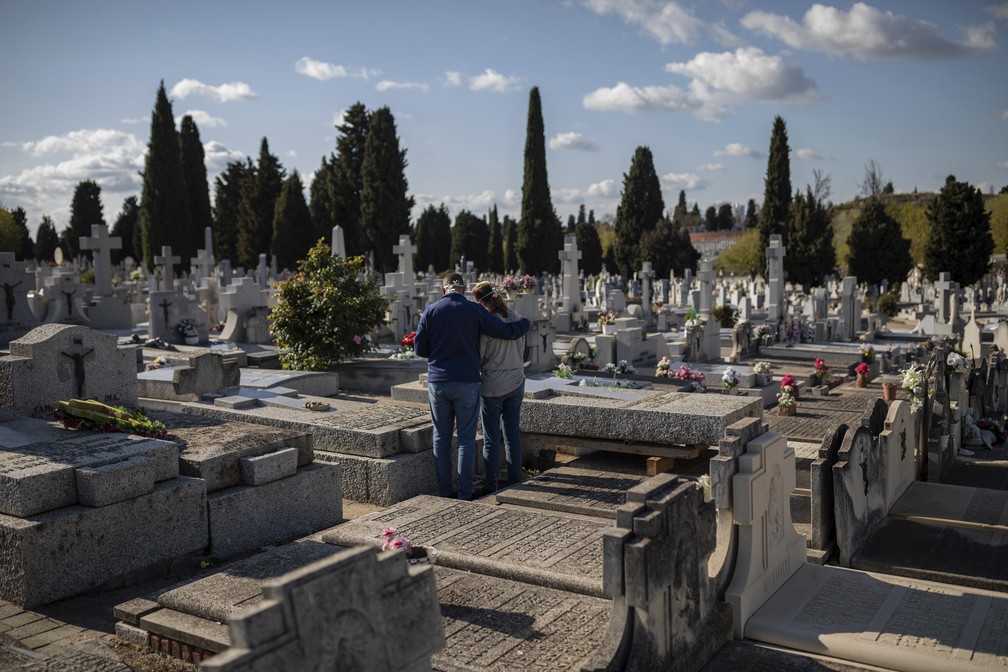 Duas pessoas usam máscaras protetoras contra a Covid-19 em um cemitério durante um enterro em Madri, na Espanha, na sexta-feira (27). O país registrou 832 mortes entre a sexta e o sábado (28). — Foto: Bernat Armangue/AP