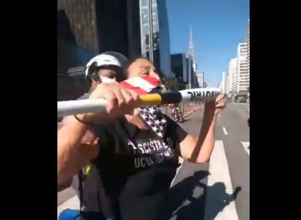 Manifestante a favor do presidente Jair Bolsonaro aponta bastão para torcedor de ato a favor da democracia e é conduzida por PM na Avenida Paulista, em São Paulo — Foto: Reprodução/Twitter