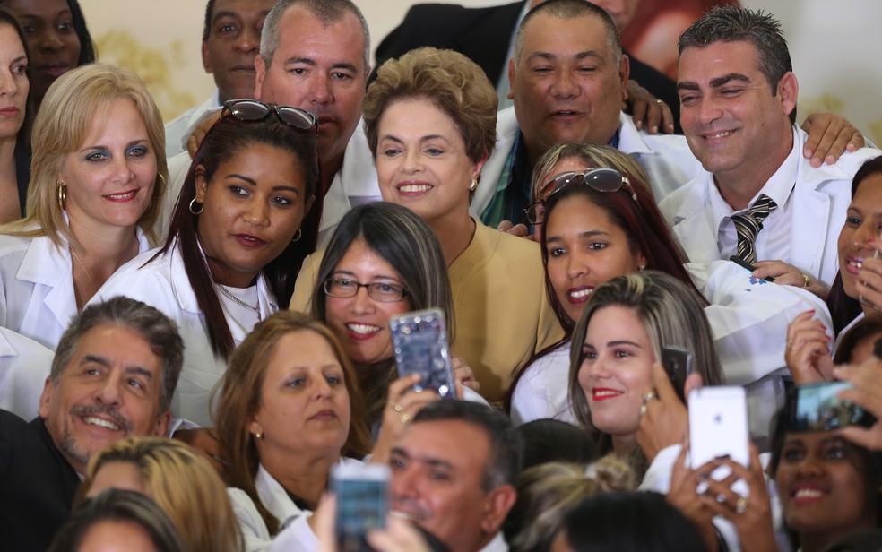 Programa Mais Médicos foi criado pelo governo de Dilma Rousseff - na imagem, tirada em 2016, Dilma lança nova fase do programa e é cercada por profissionais, alguns cubanosA presidente Dilma Rousseff anúnciou nesta sexta (29) a prorrogação do Programa Mais Médicos — Foto: Dida Sampaio/Estadão Conteúdo