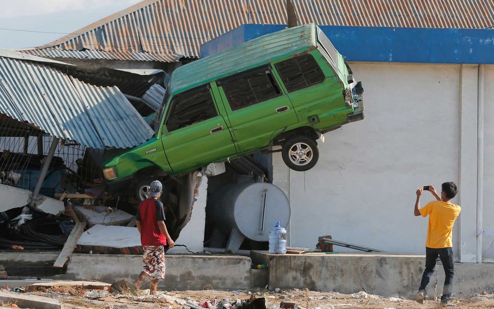 Rapaz tira foto de um carro erguido pelo tsunami — Foto: Tatan Syuflana / AP 