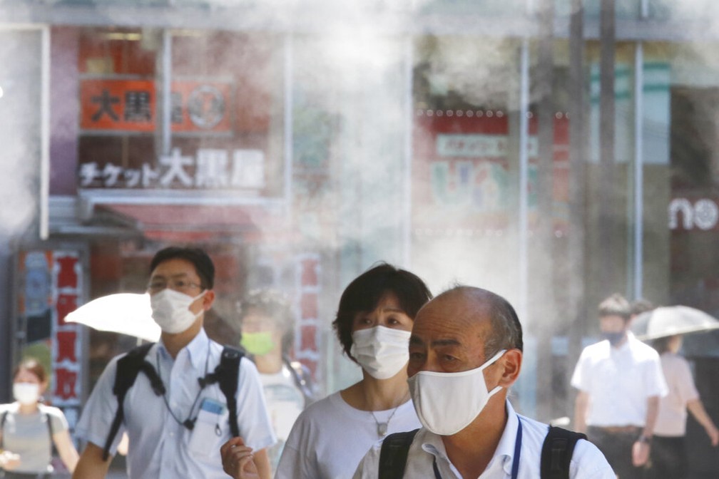 De máscaras, pessoas passam por vapor de água diante do calor em Tóquio, capital do Japão, nesta quinta (5) — Foto: Koji Sasahara/AP Photo