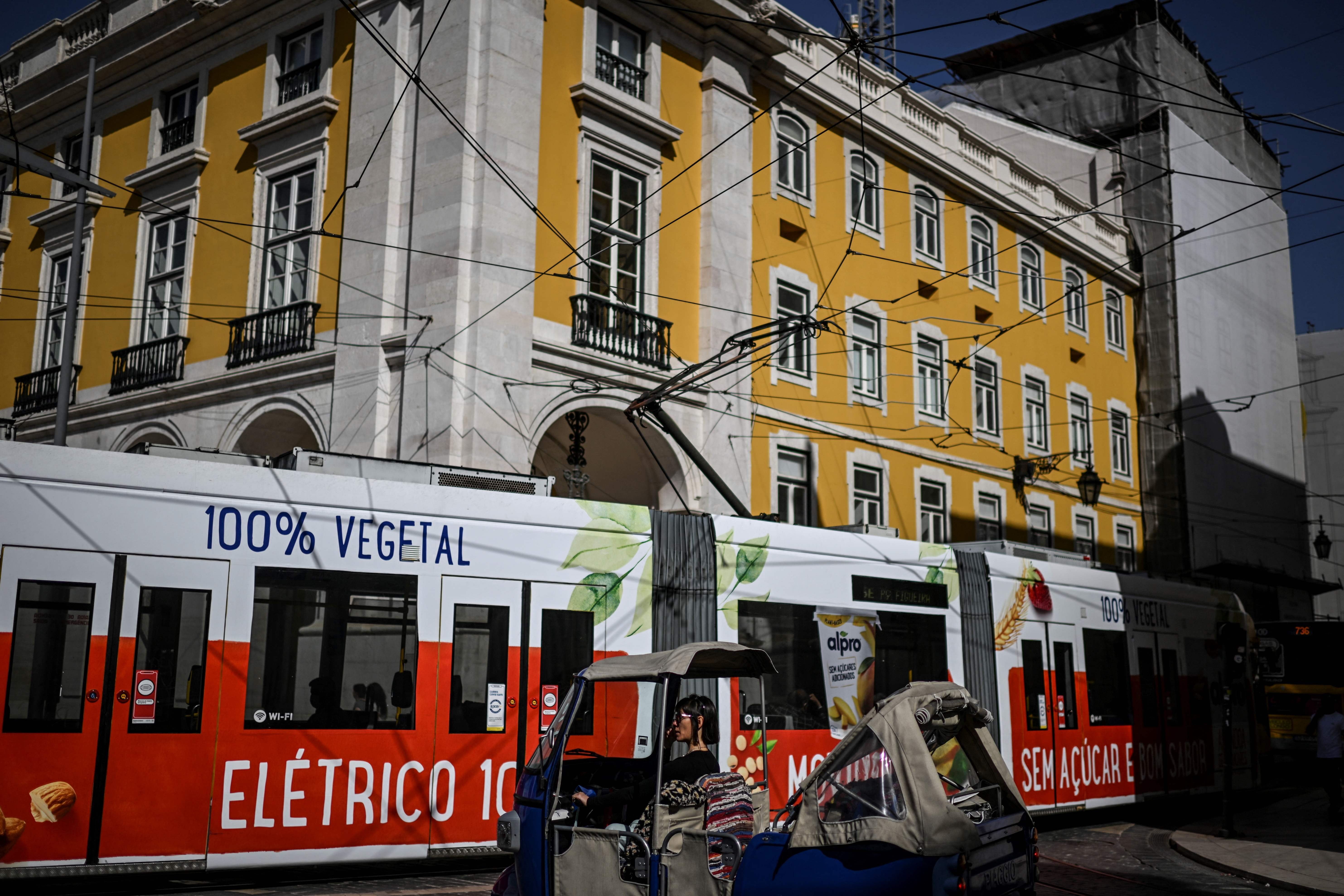 No comando de um tuk tuk, mulher aguarda o elétrico cruzar rua no centro de Lisboa