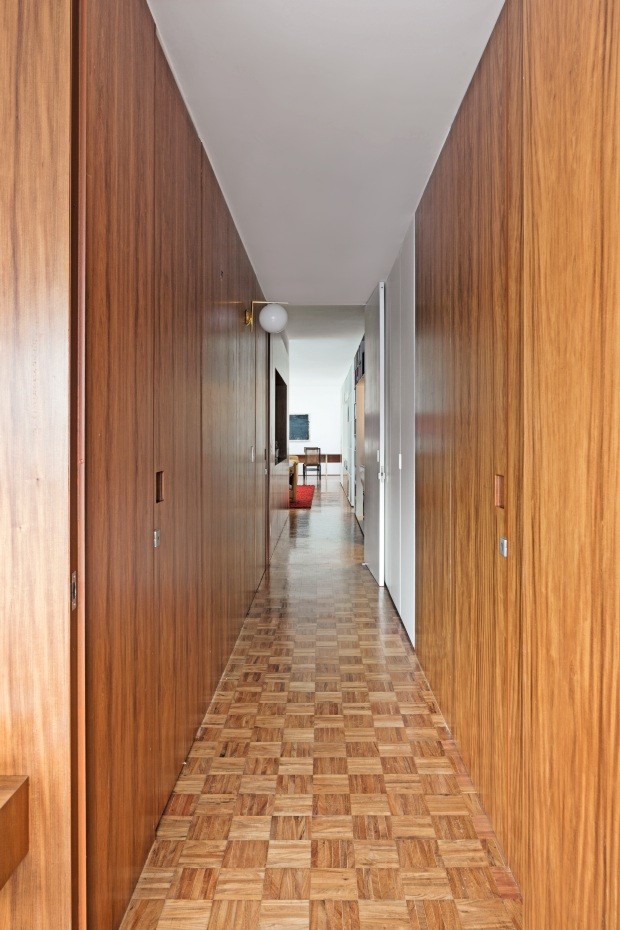 Circulação | Inseridas no painel de cabreúva, as portas pivotantes dos quartos têm puxador quadrado recortado na marcenaria. Arandela IC C/W, da FLOS (Foto: Filippo Bamberghi / Divulgação)