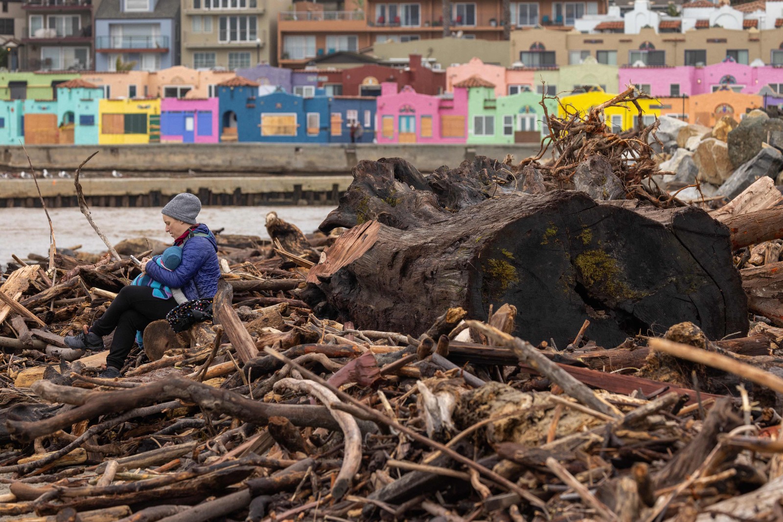 Mulher se senta com seu bebê entre árvores que foram varridas para o oceano por tempestades recentes em Capitola, Califórnia — Foto: DAVID MCNEW / AFP