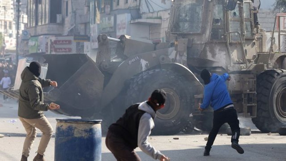 Palestinos jogam pedras em meio a confrontos com tropas israelenses durante um ataque em Jenin — Foto: EPA via BBC