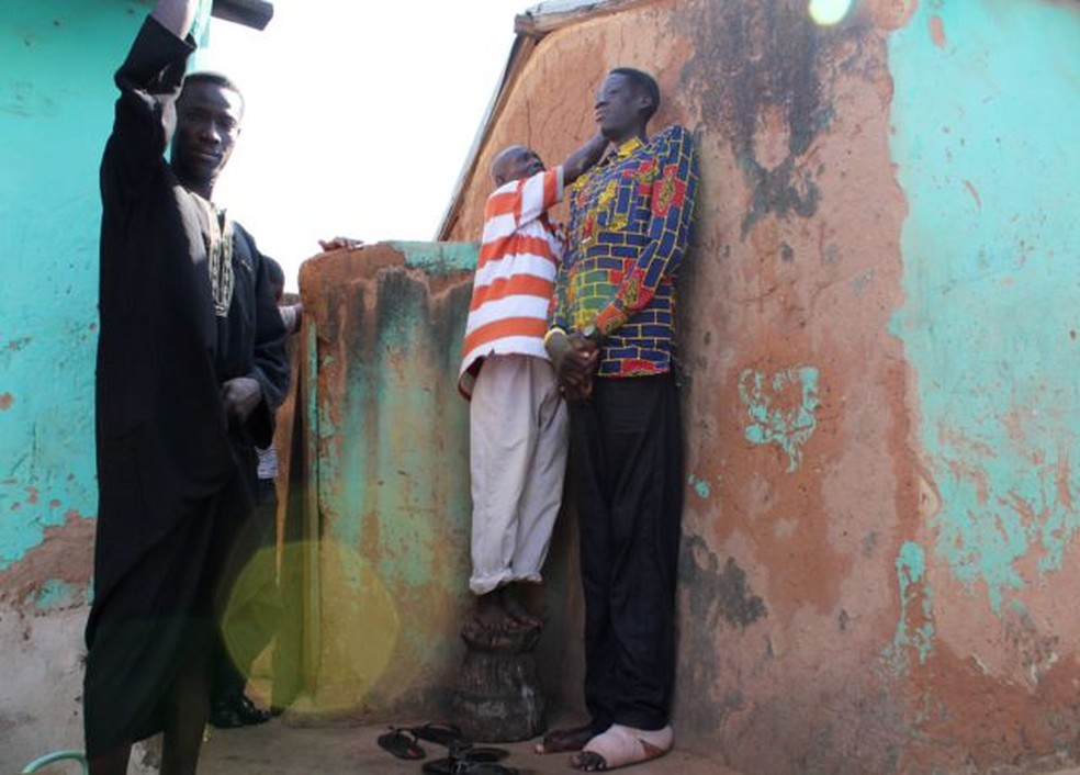 Um vizinho subiu em um banquinho para marcar a parede ao medir a altura de Awuche — Foto: BBC