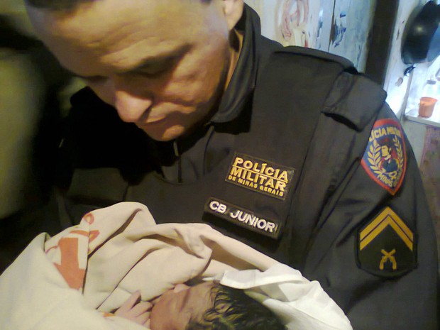Cabo Júnior segurando o bebê após o parto realizado em casa por policiais (Foto: Polícia Militar)