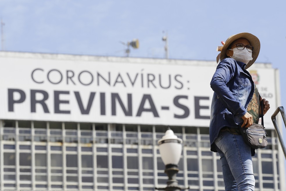 Mulher usando máscara de proteção facial passa diante de um cartaz com alerta sobre o coronavírus na região central de São Paulo — Foto: NELSON ANTOINE/ESTADÃO CONTEÚDO