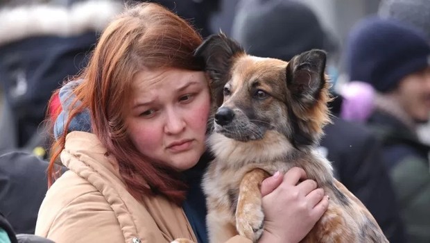 Jovem abraça seu cachorro enquanto eles aguardam para cruzar a fronteira entre a Ucrânia e a Polônia (Foto: Getty Images via BBC)