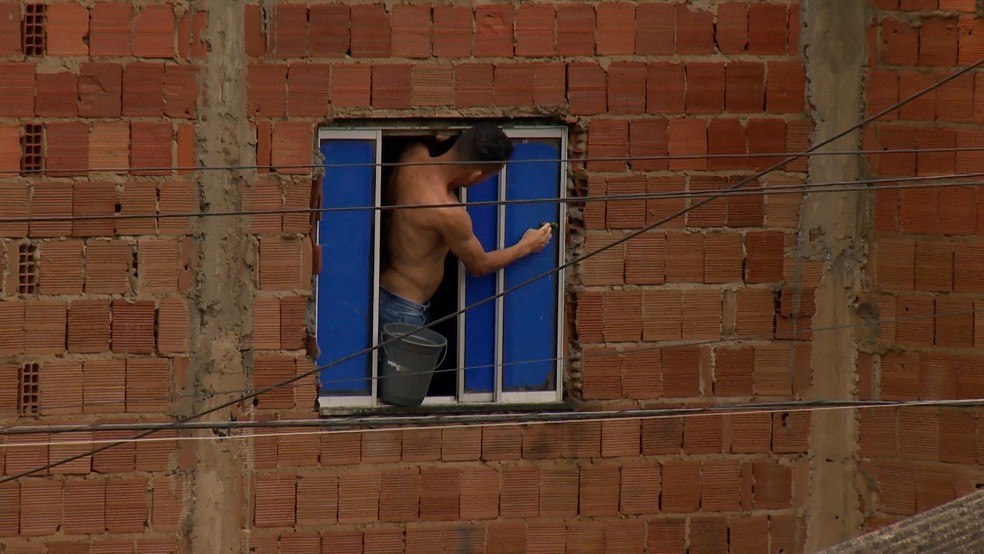 Morador tenta vedar janela no segundo andar de uma casa para evitar que água da chuva entre na residência — Foto: Reprodução/TV Gazeta