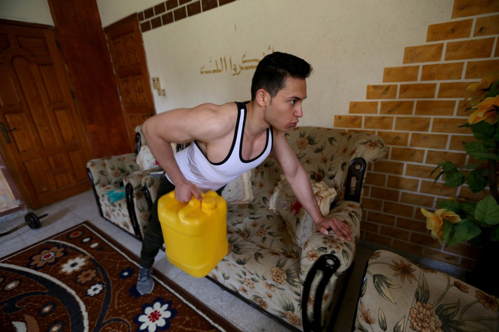 O atleta palestino Atta Saker usa um recipiente de água como peso enquanto treina em sua casa durante a quarentena para evitar a propagação da doença por coronavírus (COVID-19) em Khan Younis, no sul da Faixa de Gaza — Foto: Ibraheem Abu Mustafa/Reuters