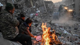 Sobreviventes queimam livros para se manter aquecidos à espera de resgate nos escombros em Hatay, Turquia — Foto: BULENT KILIC/AFP