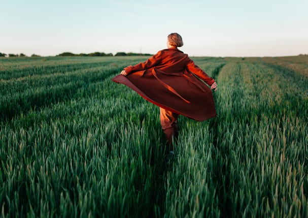 Young Caucasian woman in red coat  walking  in the field at sunset (Foto: Getty Images)