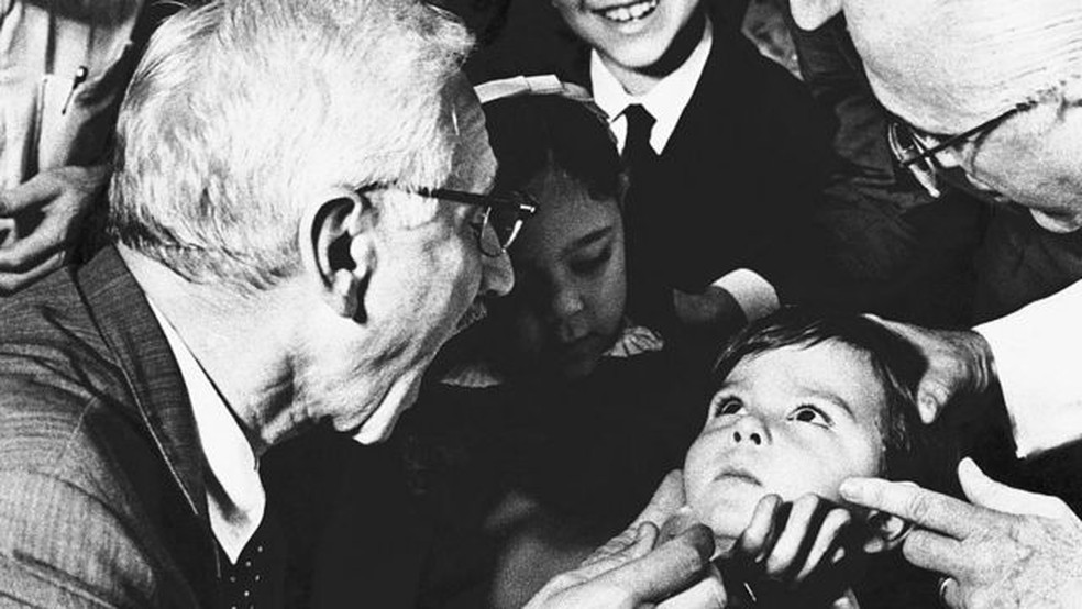 Albert Sabin, médico pesquisador que desenvolveu a vacina oral contra a poliomielite, pede ao menino Luiz Inácio Gama, de cinco anos, que abra bem a boca no hospital antipoliomielite Jesus, no Rio de Janeiro, em 1967 — Foto: Getty Images