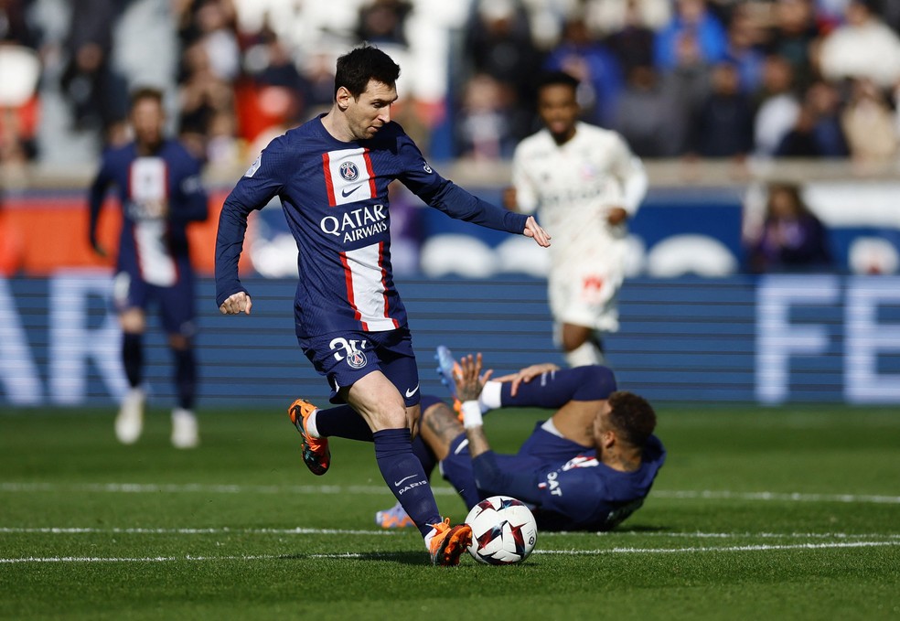 Messi com a bola, enquanto Neymar cai no gramado sentindo dores. — Foto: REUTERS