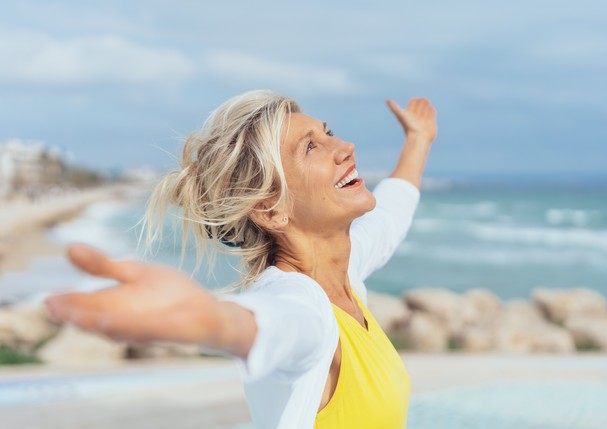 Joyful woman enjoying the freedom of the beach standing with open arms and a happy smile looking up towards the sky (Foto: Getty Images/iStockphoto)