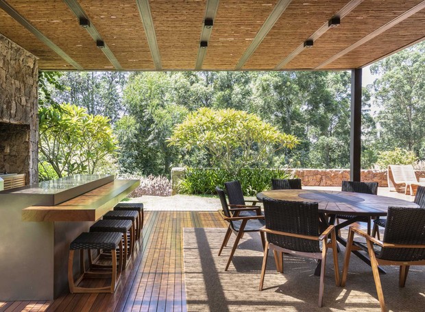 VARANDA | Integrada à sala de estar, a varanda com churrasqueira segue o conceito da casa, com muita madeira e pedras (Foto: Evelyn Muller / Divulgação)