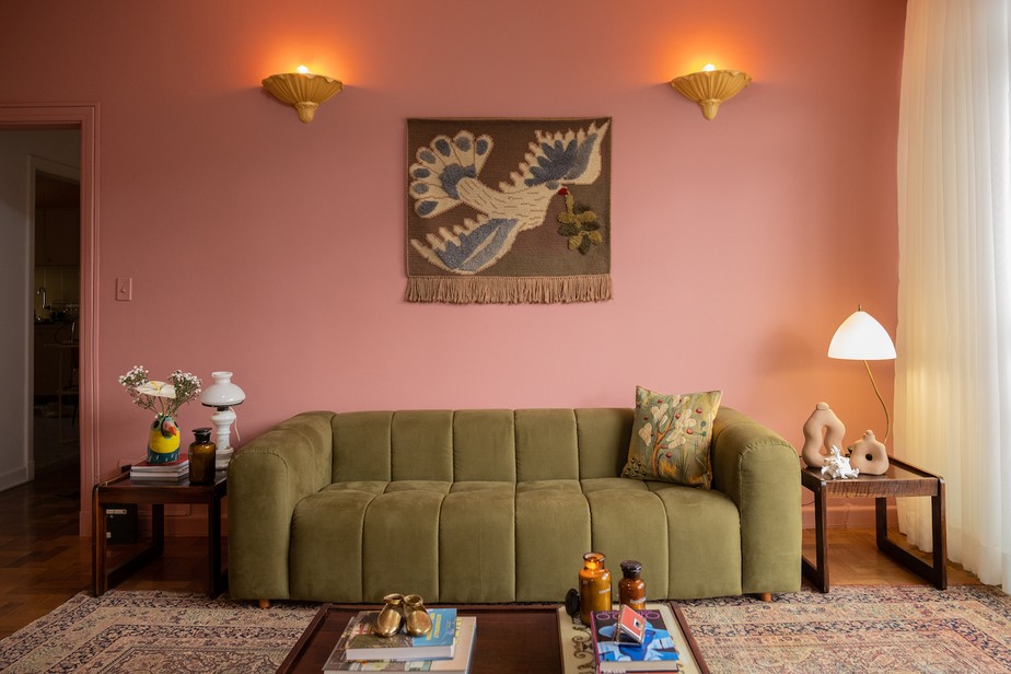 A parede rosa que emoldura o sofá verde musgo é um dos destaques da sala de estar