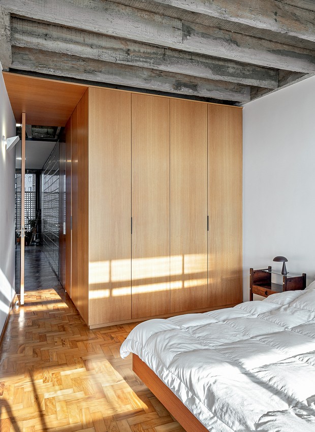 No quarto do casal, a porta pivotante e os armários integram o volume de marcenaria folhado de curupixá feito por Arno Leonhardt (Foto: André Scarpa / Divulgação)