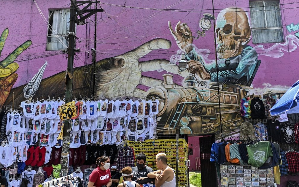 Pessoas com máscaras passam por mercado em frente a mural no mercado das pulgas de El Chopo, na Cidade do México, no dia 25 de julho. — Foto: Pedro Pardo/AFP