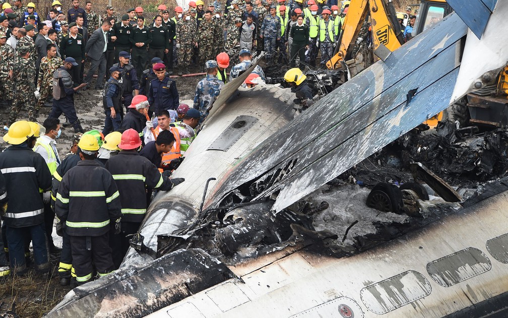 Funcionários trabalham entre os destroços do avião da US-Bangla Airlines que caiu no aeroporto de Katmandu, no Nepal, na segunda-feira (12) (Foto: Prakash Mathema/AFP)