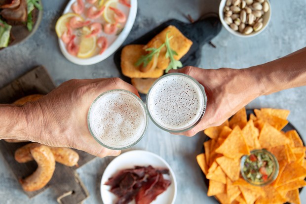Top view of two hands with beer glasses and delicious snacks. Sausages and sauces, chips, meat, shrimp with lemon. Concept of drinks, fun, food, celebrating, meeting, oktoberfest. (Foto: Freepik)