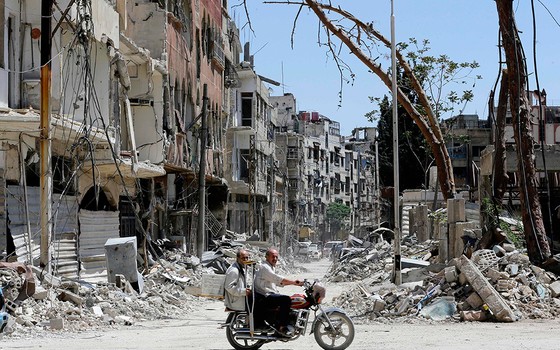 Sírios andam de moto ao longo de uma rua destruída em Douma. Exército sírio declarou que todas as forças antirregime deixaram oleste de Ghouta, após uma ofensiva de dois meses contra os rebeldes (Foto: LOUAI BESHARA/AFP)