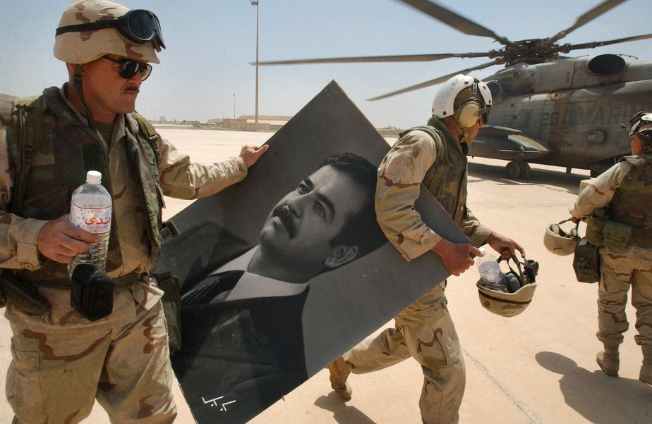 Soldados da Marinha dos EUA carregam um retrato do recém derrubado presidente iraquiano Saddam Hussein no dia 14 de abril de 2003