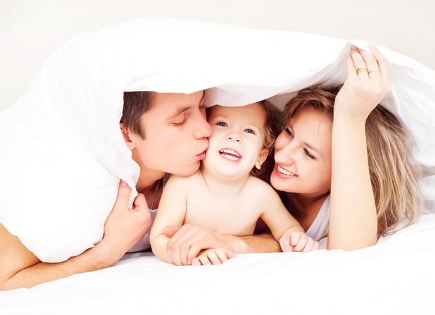 Criança na cama com os pais (Foto: Shutterstock)