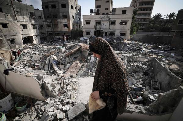 Mulher palestina verifica os danos enquanto caminha pelos escombros em frente à sua casa, na cidade de Gaza, após um cessar-fogo entre israelenses e militantes palestinos