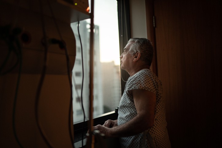 Senior patient looking through window at hospital (Foto: Getty Images)