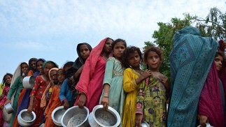 Paquistaneses afetados pelas enchentes fazem fila para receber alimentos distribuídos pela Saylani Welfare Trust em um acampamento improvisado em Sehwan, na província de Sindh  — Foto: HUSNAIN ALI/AFP