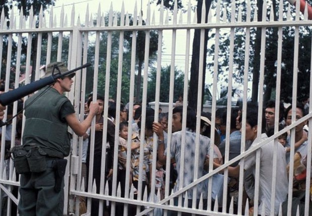 Fuzileiros navais dos EUA vigiam a entrada da embaixada em Saigon, enquanto uma multidão de vietnamitas espera para ser retiradas do país em 29 de abril de 1975 (Foto: Getty Images via BBC)