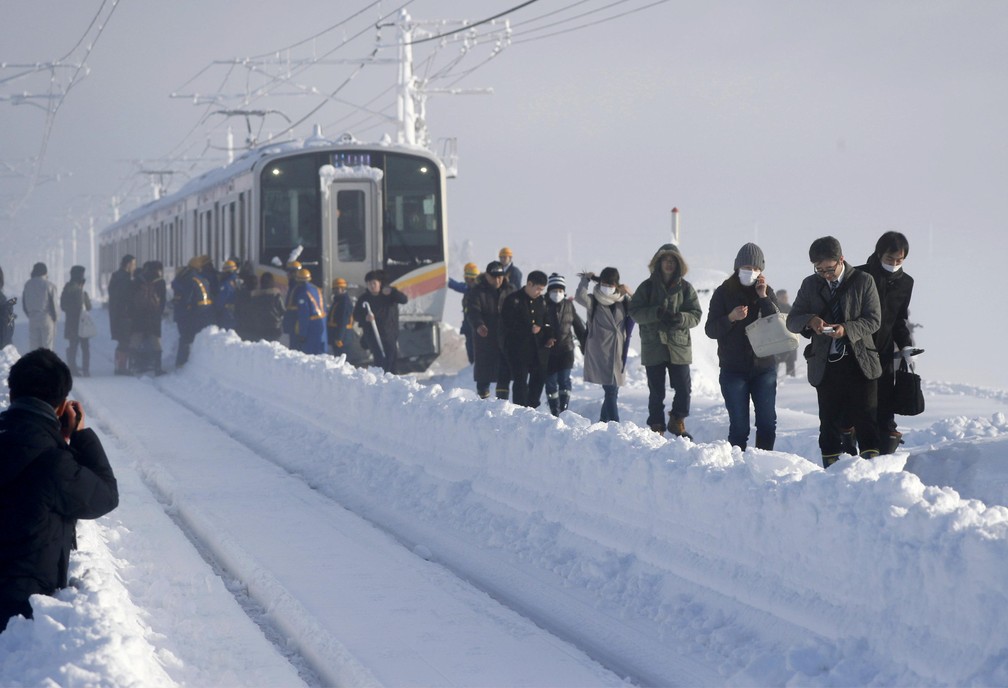 Passageiros caminham depois de sair de um trem que ficou preso por causa da neve em Sanjo, na região de Niigata, no Japão (Foto: Kyodo/via Reuters)