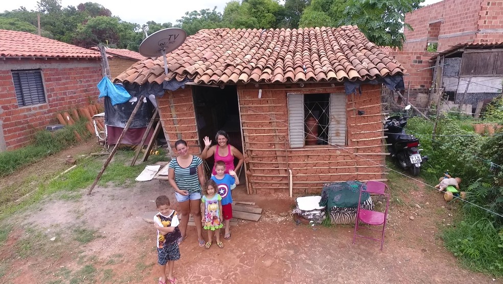 Isaac, a mãe, a tia e os irmãos diante da casa de taipa na Zona Sul da capital.  — Foto: Magno Bonfim/TV Clube