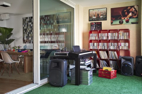 Varanda com grama sintética da Soccer Grass, equipamento de som, caixas de som, teclado, ao fundo estante com discos vinil e CDs. Projeto da arquiteta Bruna Riscali