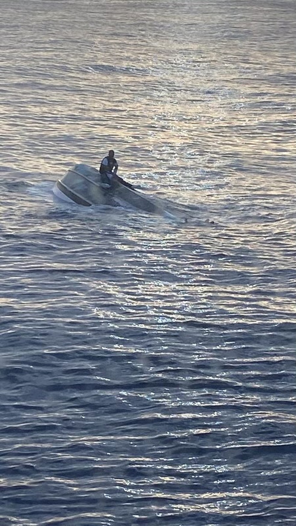 Homem que diz ser 1 das 40 pessoas que deixaram Bimini, nas Bahamas, no sábado (22), senta-se em um barco virado na costa de Fort Pierce Inlet, na Flórida, nos Estados Unidos, em foto divulgada pela Guarda Costeira dos EUA em 25 de janeiro de 2022 — Foto: Guarda Costeira dos EUA via Reuters