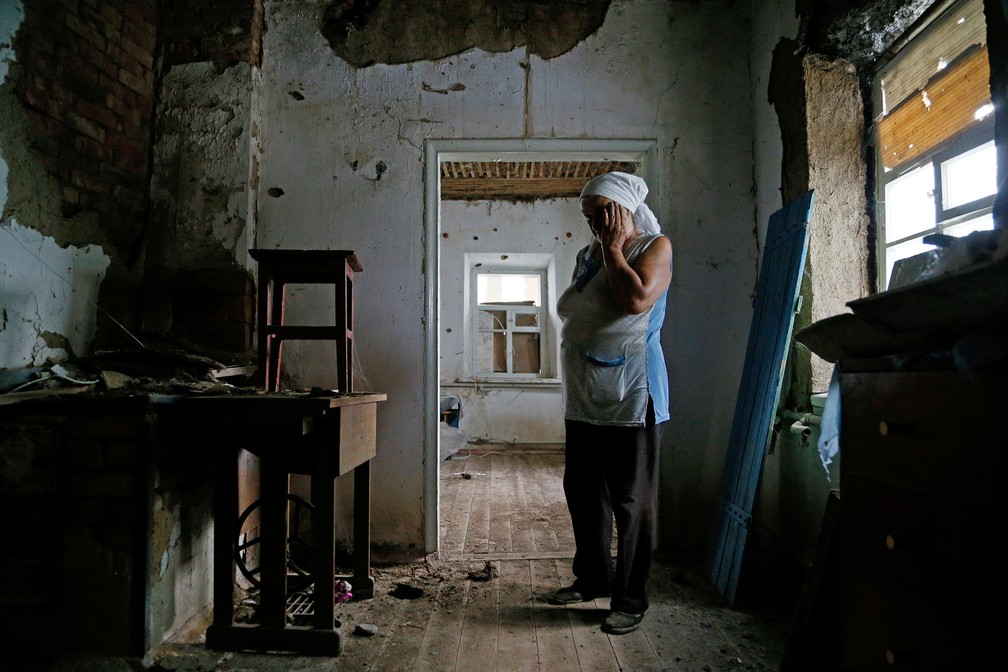 27 de julho - A moradora Katerina Izvekova mostra sua casa danificada durante conflito militar em Vesele, na região de Donetsk, Ucrânia — Foto: Alexander Ermochenko/Reuters