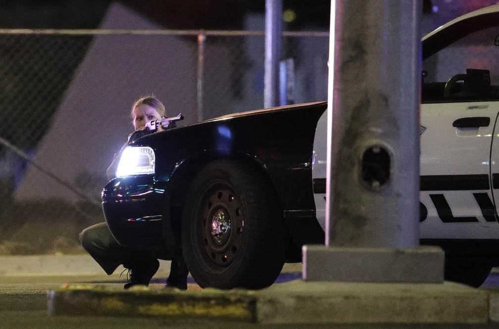 Policial se protege atrás de viatura da polícia no momento em que tiros são ouvidos perto do resort e casino Mandalay Bay, em Las Vegas Strip (Foto: John Locher/AP)