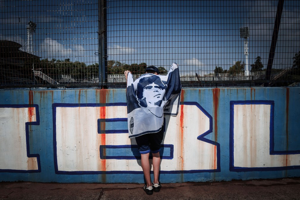 Torcedor enrolado em bandeira vai ao estádio do Gimnasia, onde Maradona dona trabalhava como treinador — Foto: Maria Paula Avila/AP Photo