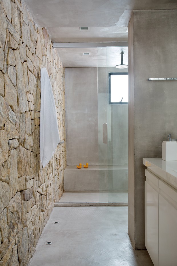 Banheiro da suíte | A parede revestida de pedra madeira é a atração do espaço, bem amplo. No boxe, banco de alvenaria (Foto: Denilson Machado/MCA Estúdio)
