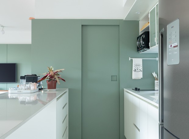 A cozinha fica aberta para a área social. No detalhe, nota-se a porta de acesso à lavanderia bem disfarçada no painel verde menta (Foto: Pedro Napolitano Prata/Divulgação)