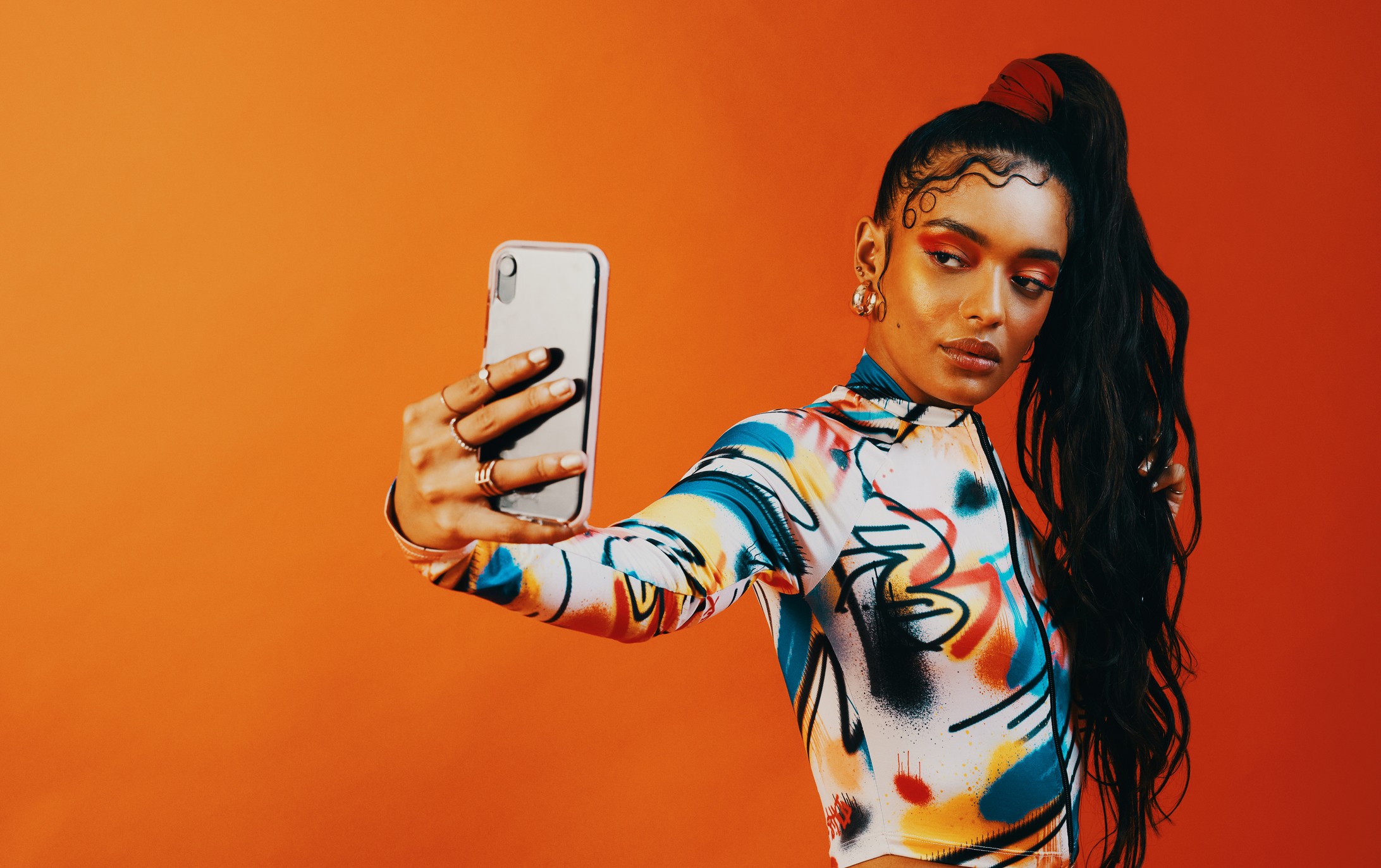 Studio shot of a fashionable woman taking a selfie against a orange background (Foto: Getty Images)